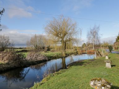 A river with trees and grass along the bank in a rural area at Stables Cottage in Bowerhill near Melksham