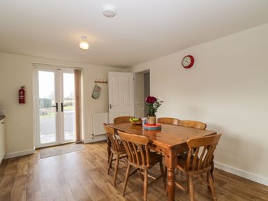 A dining room with a wooden table and six chairs and glass doors opening to outside at Stables Cottage in Bowerhill near Melksham
