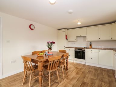 A kitchen with wooden dining table and chairs with flowers and fruit on the table at Stables Cottage in Bowerhill near Melksham