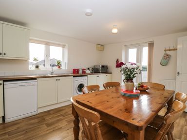 A kitchen with wooden dining table and chairs washing machine and dishwasher under countertop at Stables Cottage in Bowerhill near Melksham