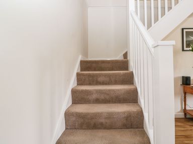 A carpeted staircase with white wooden railing next to a wall at Stables Cottage in Bowerhill near Melksham