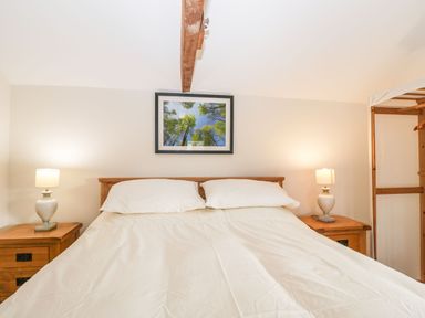 A bedroom with a double bed two bedside tables and lamps a framed picture on the wall and wooden beam on the ceiling at Stables Cottage in Bowerhill near Melksham