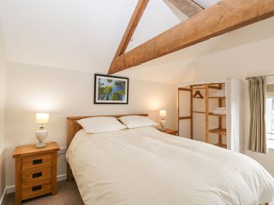 A bedroom with a double bed side tables lamps a wooden open wardrobe and a window with curtains at Stables Cottage in Bowerhill near Melksham