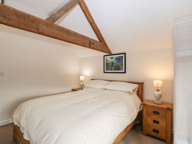 A bedroom with a wooden bed frame bedside tables lamps and a framed picture on the wall at Stables Cottage in Bowerhill near Melksham