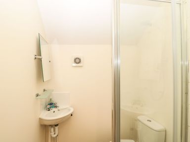 A small bathroom with a wall-mounted sink mirror shower enclosure and toilet at Stables Cottage in Bowerhill near Melksham