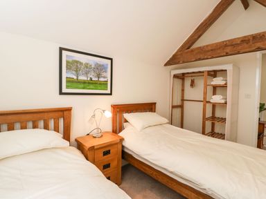 A bedroom with two single beds a wooden nightstand a lamp and an open wardrobe at Stables Cottage in Bowerhill near Melksham