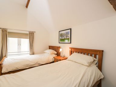 A bedroom with two single beds a wooden nightstand and a window with curtains at Stables Cottage in Bowerhill near Melksham