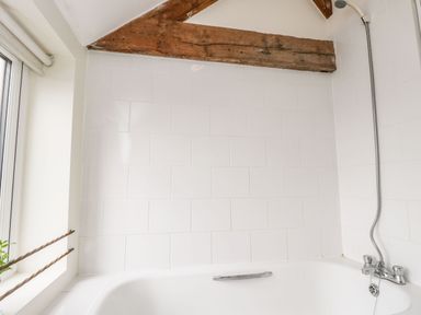 A bathroom with white tiled walls a bathtub a showerhead and a window with a small plant at Stables Cottage in Bowerhill near Melksham