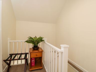 A stair landing with a wooden side table holding a potted plant and a wooden luggage rack at Stables Cottage in Bowerhill near Melksham