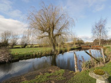 A river with trees and grassy banks at Stables Cottage in Bowerhill near Melksham