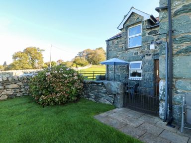 A patio area with a stone wall and grass at Tyddyn in Dyffryn Ardudwy