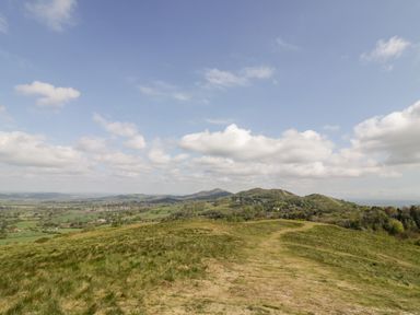 A grassy hill with a dirt path and distant hills under a partly cloudy sky at Beesoni Lodge in Castlemorton near Malvern