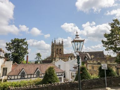 A view of historic buildings with a church tower trees and a street lamp with a road sign for Ledbury and Colwall at Beesoni Lodge in Castlemorton near Malvern