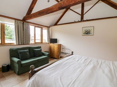 A bedroom with a bed a green sofa a wooden cabinet with a television and exposed wooden ceiling beams at Beesoni Lodge in Castlemorton near Malvern