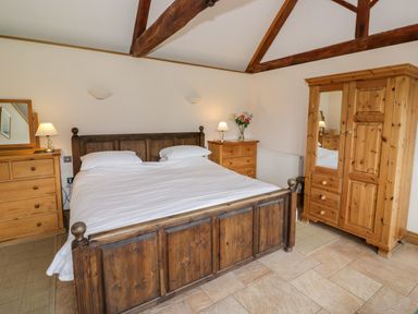 A bedroom with a wooden bed and matching furniture with lamps and flowers at Beesoni Lodge in Castlemorton near Malvern