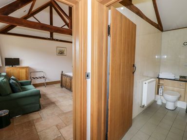 A living area with a green sofa and television next to a bathroom with a toilet and towels at Beesoni Lodge in Castlemorton near Malvern