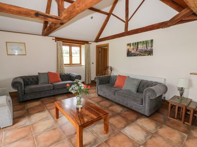 A living room with two grey sofas a wooden coffee table with flowers and exposed wooden beams at Beesoni Lodge in Castlemorton near Malvern