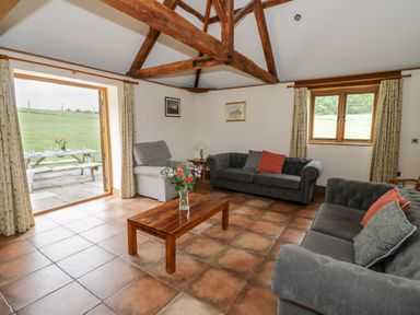 A living room with two gray sofas a gray armchair wooden coffee table with flowers exposed wooden beams and patio doors open to a garden at Beesoni Lodge in Castlemorton near Malvern