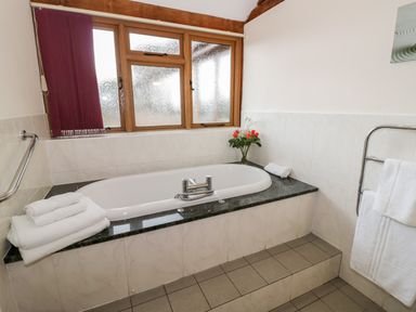 A bathroom with a bathtub surrounded by tiles and a marble ledge with towels and flowers at Beesoni Lodge in Castlemorton near Malvern