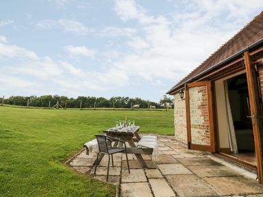 A stone patio with a wooden picnic table and chairs outside a stone house at Beesoni Lodge in Castlemorton near Malvern