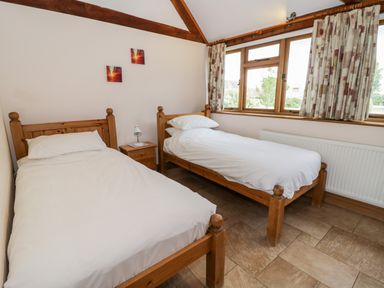 A bedroom with two single beds a wooden nightstand between the beds and curtained windows at Beesoni Lodge Castlemorton near Malvern