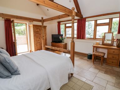 A bedroom with a four-poster bed wooden wardrobe TV dresser and dressing table at Beesoni Lodge in Castlemorton near Malvern
