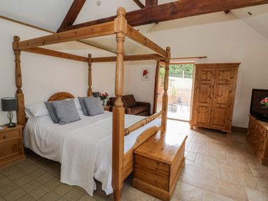 A bedroom with a wooden four-poster bed a wooden chest a wooden wardrobe a sofa and a television at Beesoni Lodge in Castlemorton near Malvern