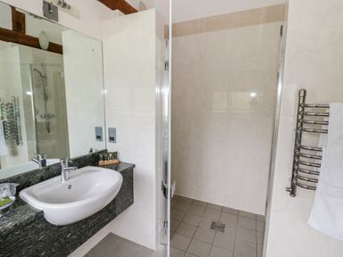 A bathroom with a sink and mirror next to a walk-in shower and a towel warmer at Beesoni Lodge in Castlemorton near Malvern