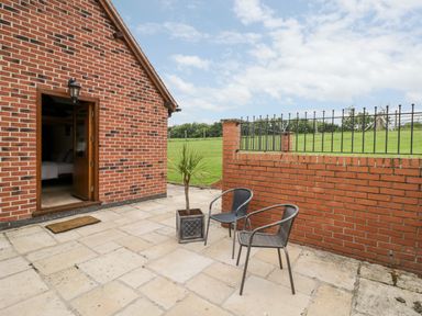 A patio with two chairs and a potted plant next to a brick wall and an open door at Beesoni Lodge in Castlemorton near Malvern