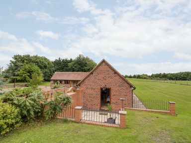 A brick house with a patio and fenced yard surrounded by grass and trees at Beesoni Lodge in Castlemorton near Malvern