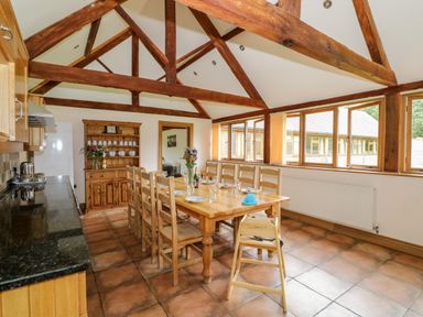 A dining area with wooden table and chairs under exposed wooden beams at Beesoni Lodge in Castlemorton near Malvern