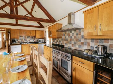 A kitchen with wooden cabinets and beams a dining table set with plates and glasses at Beesoni Lodge Castlemorton near Malvern