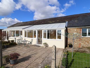 A patio with a metal table and two chairs in front of a conservatory attached to a stone house at 1 Cowdea Farm in Bettiscombe near Beaminster and Bridport