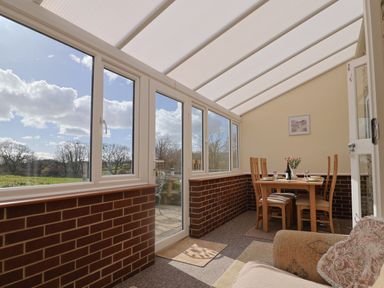 A sunroom with dining table and chairs and windows showing outdoor trees at 1 Cowdea Farm in Bettiscombe near Beaminster and Bridport