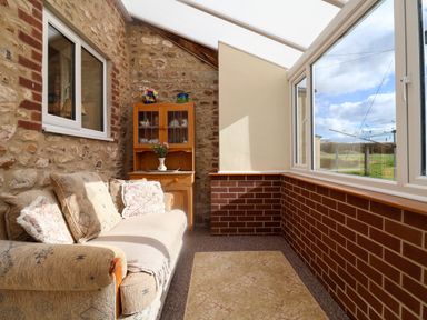 A sunroom with a sofa and a wooden cabinet with glass doors at 1 Cowdea Farm Bettiscombe near Beaminster and Bridport