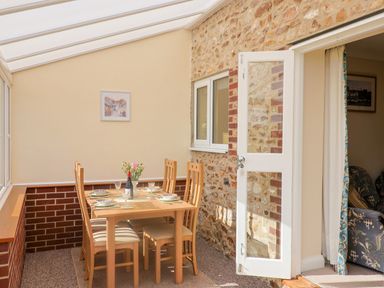 A dining area with a wooden table and six chairs set with plates glasses and a wine bottle at 1 Cowdea Farm in Bettiscombe near Beaminster and Bridport