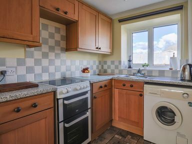 A kitchen with wooden cabinets a double oven an electric stove a washing machine a sink under a window and tiled walls at 1 Cowdea Farm Bettiscombe near Beaminster and Bridport