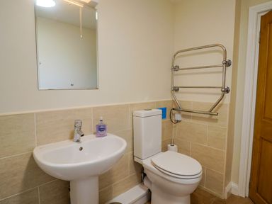 A bathroom with a white sink and faucet a mirror a toilet with a toilet paper roll and a metal towel rack on the wall at 1 Cowdea Farm in Bettiscombe near Beaminster and Bridport