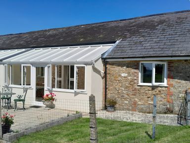 An exterior view of a stone and white house with a glass conservatory and outdoor furniture at 1 Cowdea Farm Bettiscombe near Beaminster and Bridport