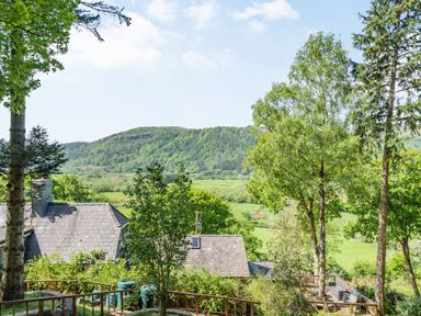 A garden with trees and outdoor seating overlooking fields and a hill at Bluebell Cottage in Maenan near Llanrwst