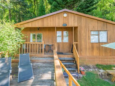 A wooden cottage with outdoor seating and lounge chairs on a deck at Bluebell Cottage in Maenan near Llanrwst