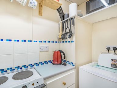 A small kitchen corner with red electric kettle white toaster stovetop and hanging kitchen utensils at Bluebell Cottage in Maenan near Llanrwst