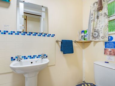 A bathroom with a white sink and a mirror above blue towel on a rack and toilet with floral curtain at Bluebell Cottage in Maenan near Llanrwst