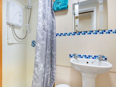 A bathroom with a shower, shower curtain, sink, mirror, and first aid box at Bluebell Cottage in Maenan near Llanrwst