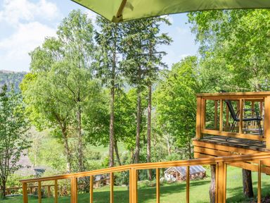 A wooden deck with chairs overlooking a green yard with trees at Bluebell Cottage in Maenan near Llanrwst