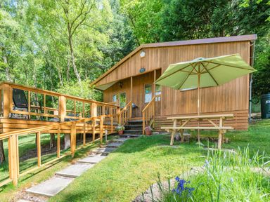 A wooden cabin with a deck and a picnic table with umbrella in a garden at Bluebell Cottage in Maenan near Llanrwst