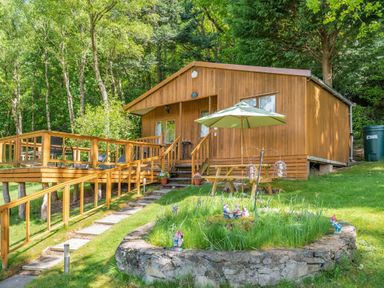 A wooden cabin with a deck and outdoor seating surrounded by trees at Bluebell Cottage in Maenan near Llanrwst