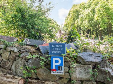 A stone wall with Bluebell Cottage parking signs and green foliage around in Maenan near Llanrwst