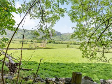 A green field with sheep and trees framing hills in the background at Bluebell Cottage in Maenan near Llanrwst