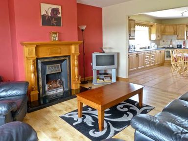A living room with a fireplace wooden coffee table and black leather sofas next to a kitchen at Sallywood House Carn near Ballybofey County Donegal